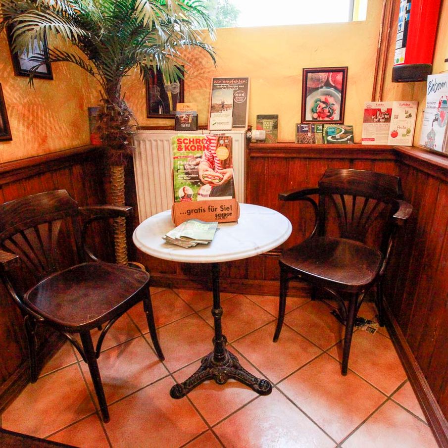 Bistrotisch mit zwei Holzstühlen vor holzvertäfelter Wand im Naturkostladen Häcklingen